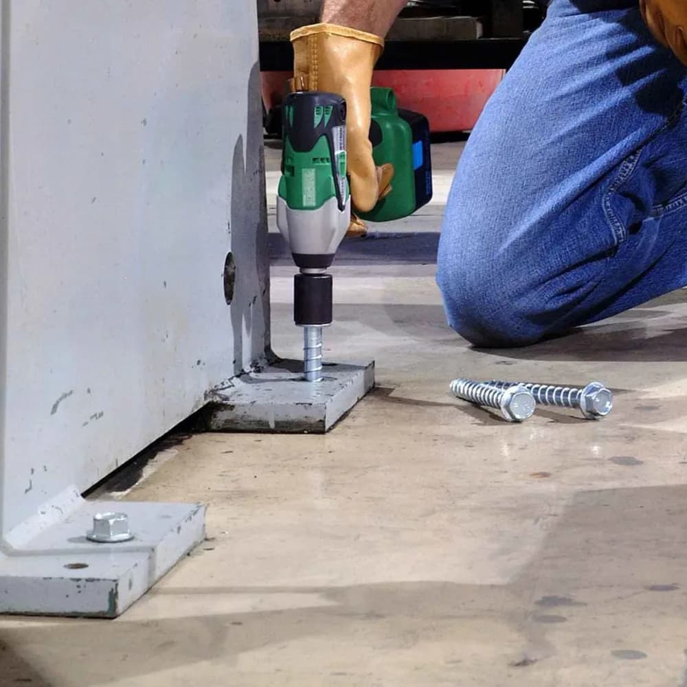 A wedge anchor being installed through a steel base plate into a concrete floor slab